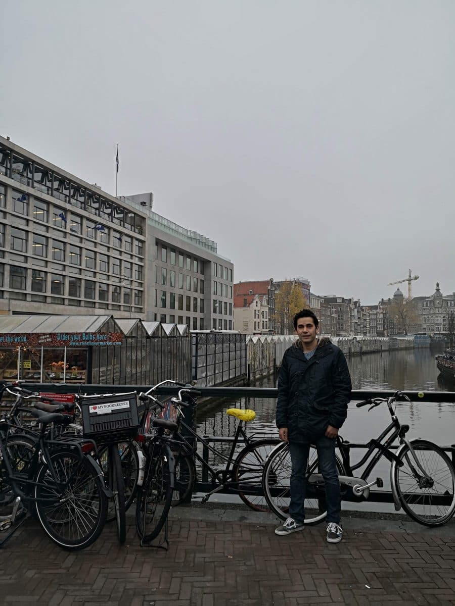 Diego Fresno standing beside bicycles locked to the railing of an Amsterdam bridge
